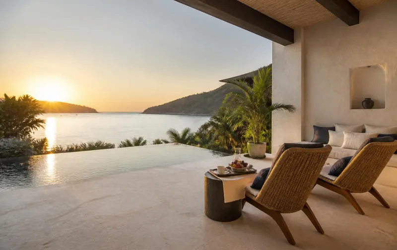A quiet private terrace for two at sunrise with woven lounge chairs, a small breakfast tray and a plunge pool overlooking a calm bay.