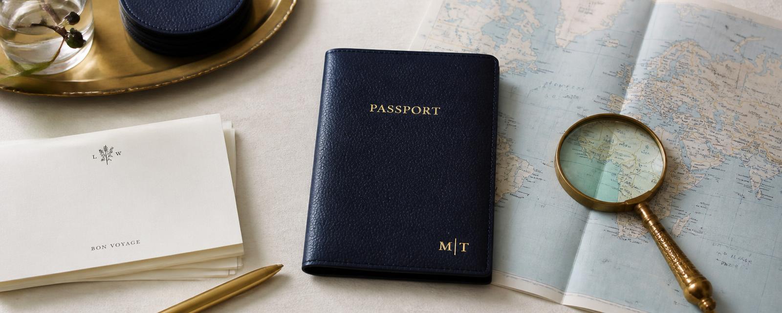 Navy leather passport folio, brass magnifier, and a folded map on an ivory desk